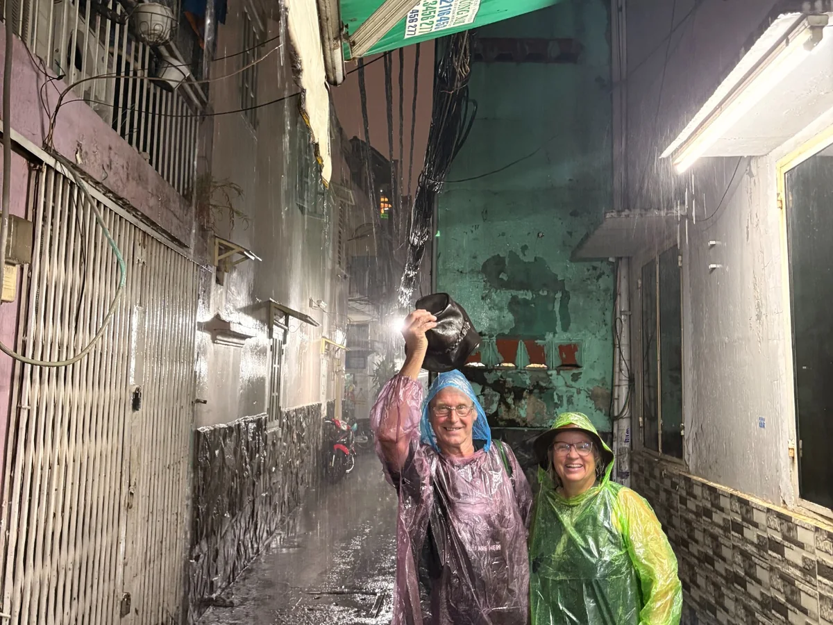 Visitors smiling in rain ponchos while exploring a narrow Saigon alley with OG Saigon