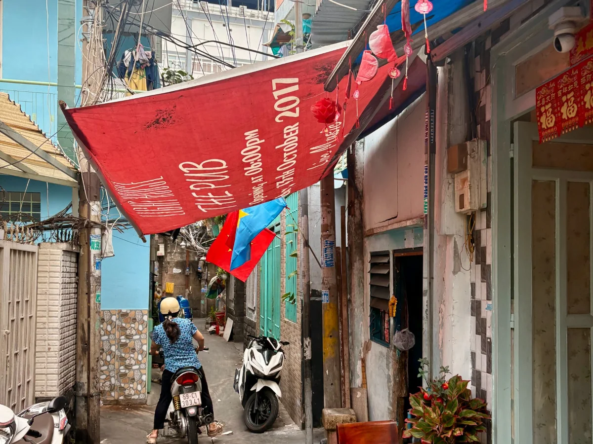 A narrow residential alley in old District 4, Saigon, with scooters, homes and hanging decorations