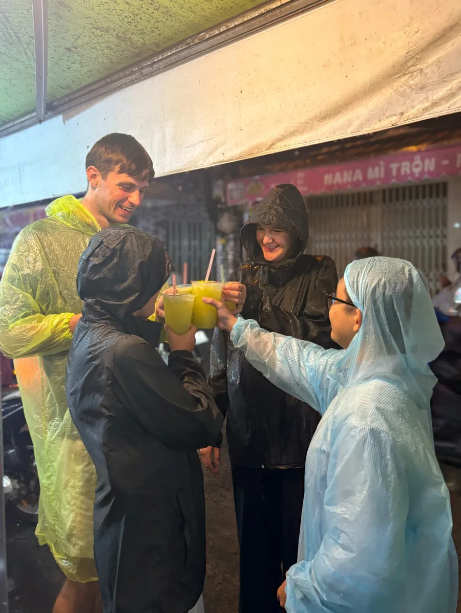 Guests sharing drinks during a rainy Saigon street-food evening
